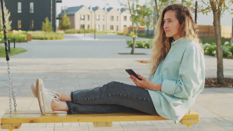 Frau-Sitzt-Auf-Schaukel-Im-Freien-Und-Benutzt-Smartphone